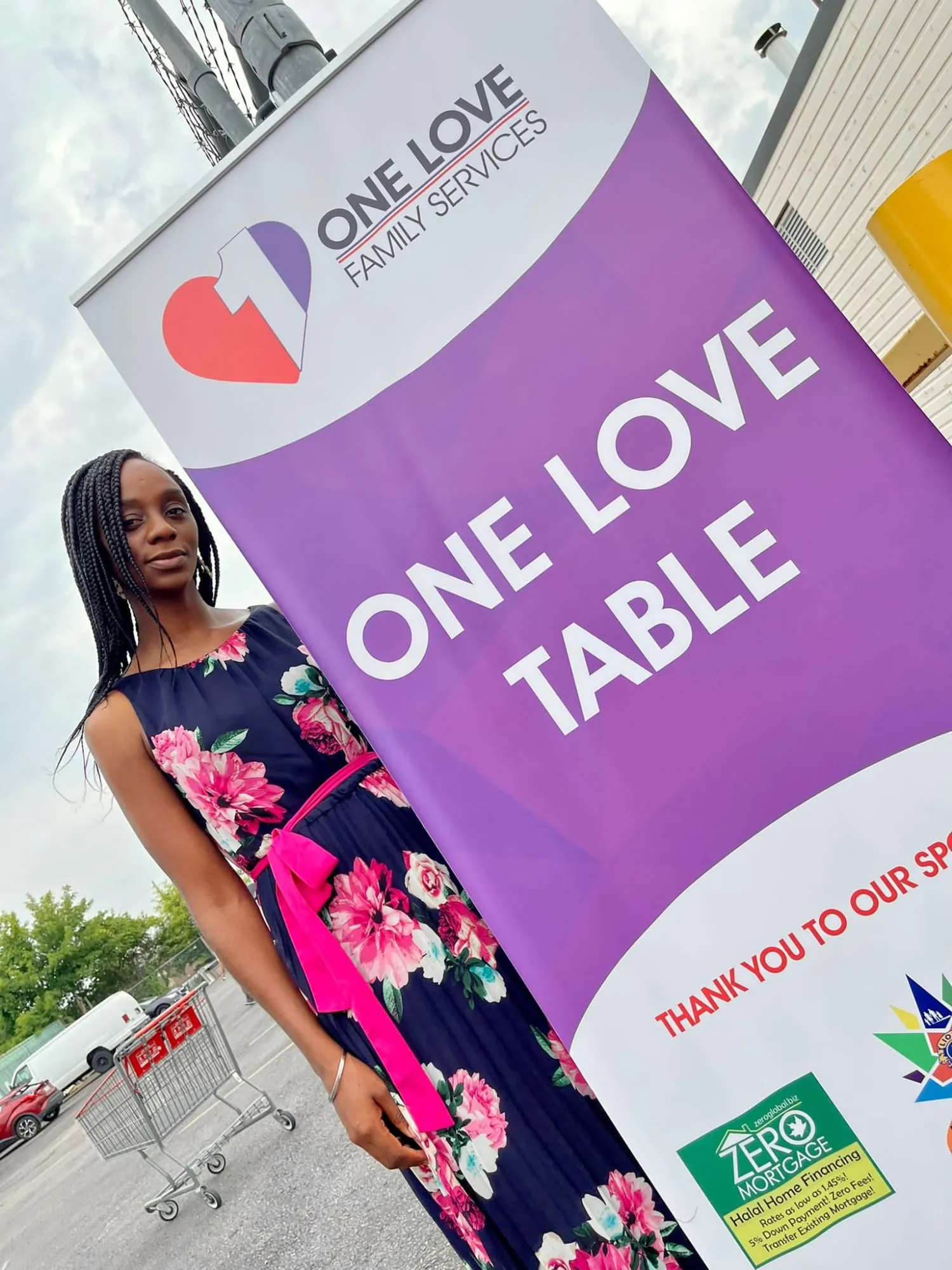 A woman standing beside the One Love Table banner at a distribution day